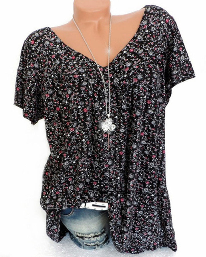 Blouse Verity pour femme à manches courtes, coupe ample et fluide avec col V, imprimé fleuri moderne noir avec petites fleurs roses et motifs blancs, portée avec un jean  look casual chic et tendance.