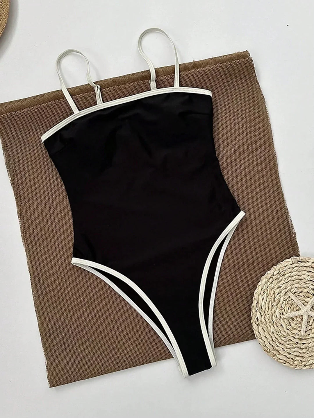 Maillot de bain une pièce noir avec des bretelles fines et des détails en contraste blanc. Design chic et minimaliste, parfait pour un look moderne à la plage ou à la piscine.