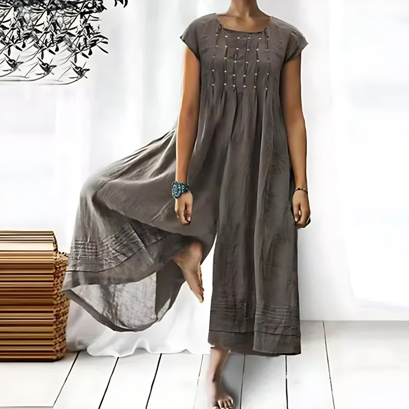 Une robe longue et fluide pour femme, de couleur grise, avec des détails de broderie délicate sur le devant, offrant une silhouette décontractée et élégante, idéale pour les journées d'été.
