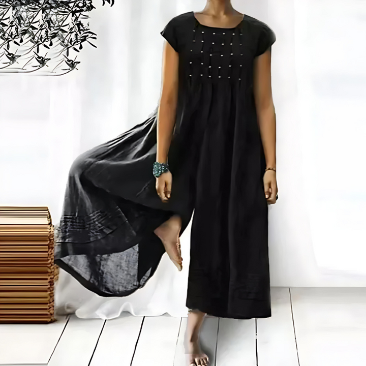 Une robe longue et fluide pour femme, de couleur noire, avec des broderies délicates sur le devant, créant une silhouette élégante et décontractée, idéale pour les occasions estivales.
