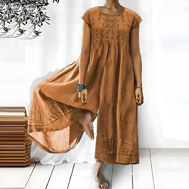 Une robe longue et fluide pour femme, de couleur marron clair, avec des broderies délicates sur le devant, créant une silhouette légère et élégante, idéale pour les journées d'été.