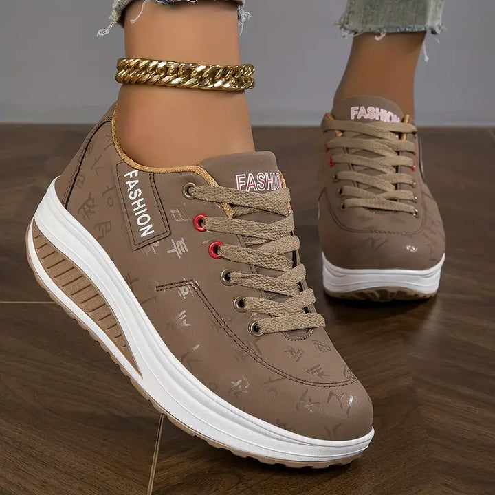Baskets plates pour femme coloris taupe, à lacets, avec détails et semelle épaisse blanche, portées avec un jean.