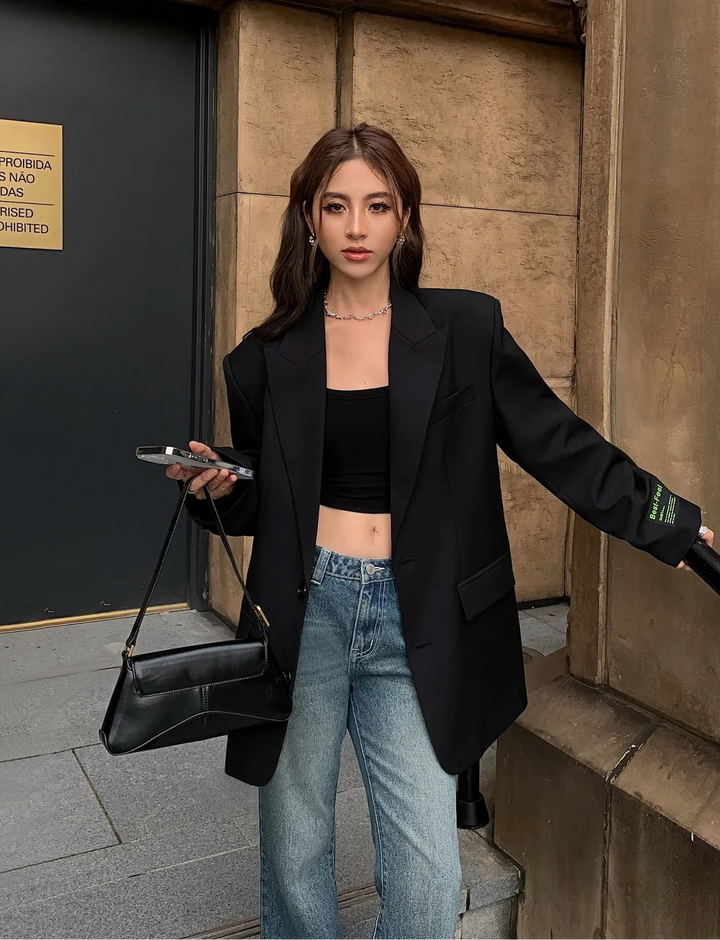 Femme portant le blazer Abella chic pour femme, veste noire oversize au style moderne, associée à un crop top noir et un jean décontracté, idéale pour un look élégant et tendance au quotidien.