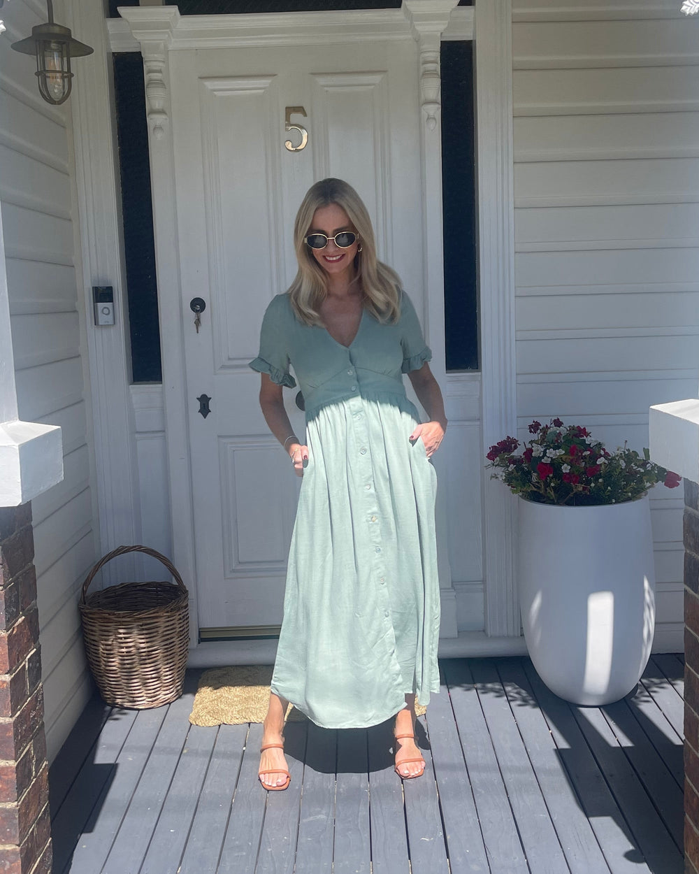 Robe midi d'été Wren pour femme, portée par une modèle devant une porte. Style tendance avec des boutons sur le devant, des manches à volants et une coupe fluide, parfaite pour une journée estivale décontractée.