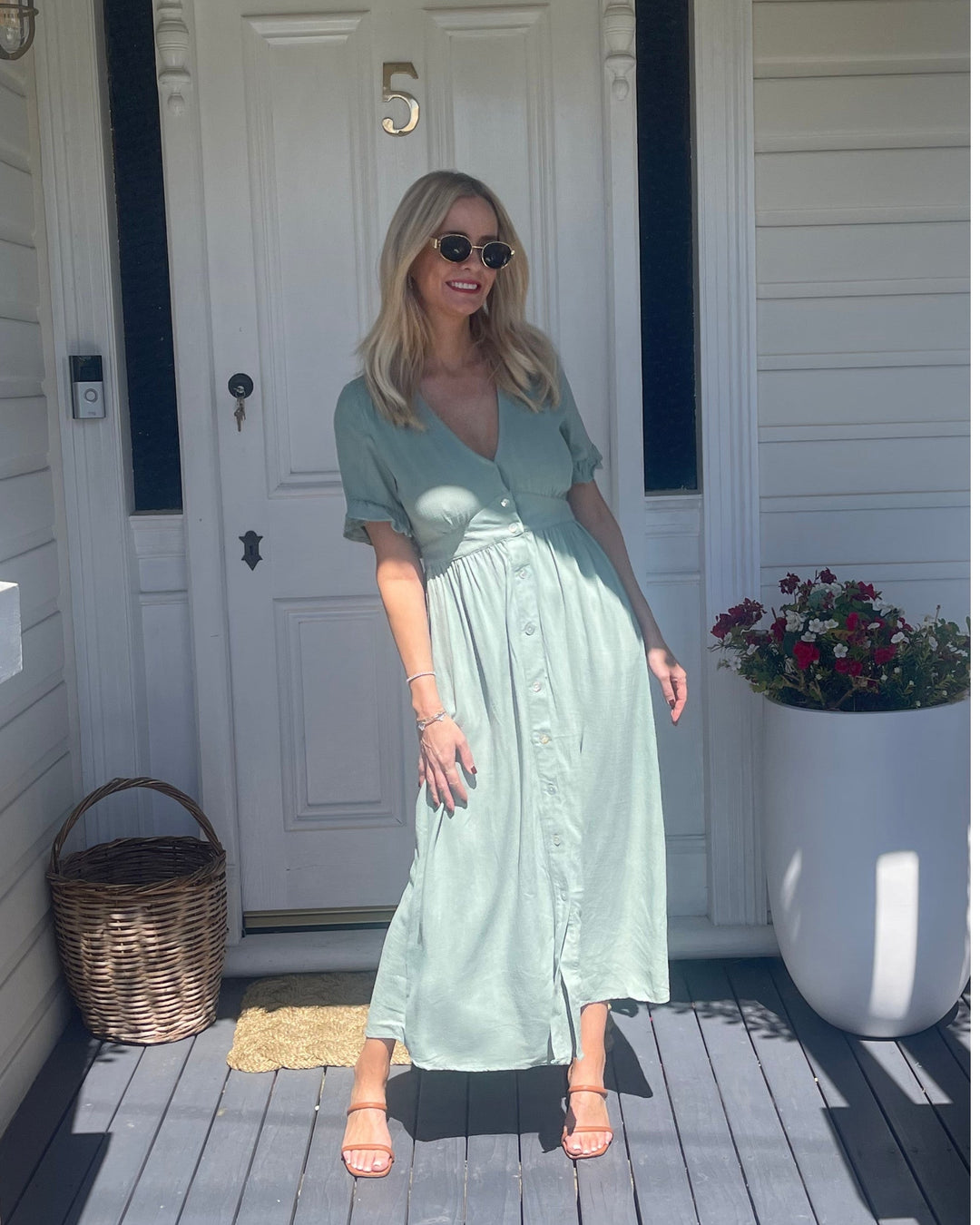 Robe midi d'été Wren pour femme, portée par un modèle devant une porte. Le design tendance avec des manches à volants, des boutons sur le devant et une coupe fluide, parfait pour un look estival chic et décontracté.
