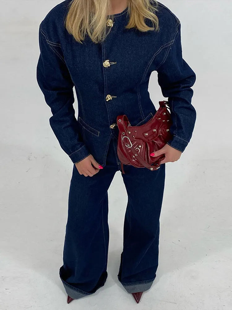 veste en jean bleu foncé à boutons dorés et pantalon assorti, look hivernal chic, elle tient un sac à main rouge bordeaux et porte des escarpins assortis.