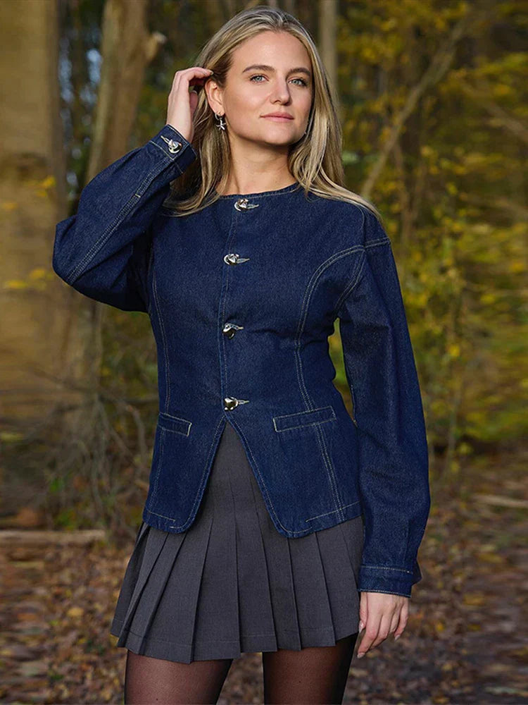 veste en jean bleu foncé à boutons argentés et jupe plissée gris, silhouette hivernale chic, photo en extérieur dans un cadre naturel.