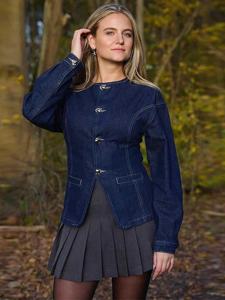 veste en jean bleu foncé à boutons argentés et jupe plissée gris, silhouette hivernale chic, photo en extérieur dans un cadre naturel.