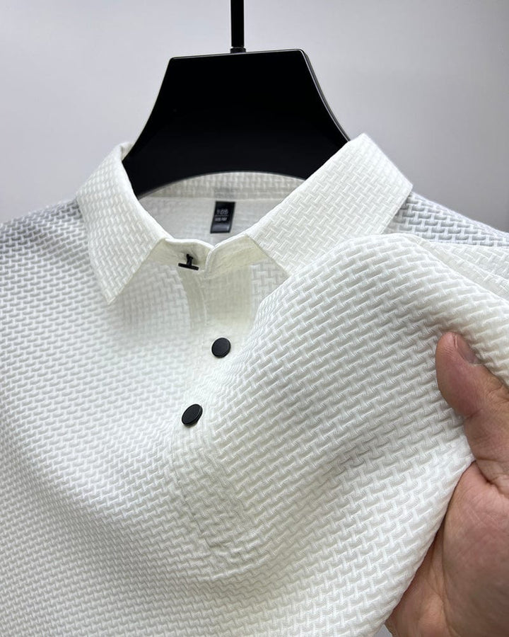 Gros plan sur un polo blanc en maille texturée, avec un col classique et des boutons noirs contrastés. Ce polo élégant et confortable offre un style moderne et décontracté, parfait pour un look raffiné et casual.