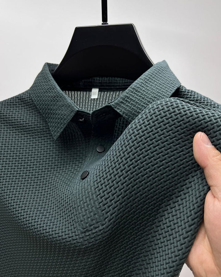 Gros plan sur un polo vert foncé en maille texturée, avec un col classique et des boutons noirs contrastés. Ce polo élégant et moderne offre à la fois confort et style, parfait pour un look décontracté et raffiné.
