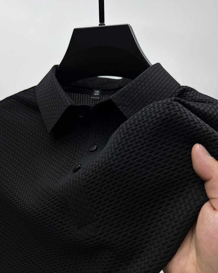 Gros plan sur un polo noir en maille texturée, avec un col classique et des boutons noirs contrastés. Ce polo élégant et moderne offre un style raffiné et décontracté, parfait pour toutes les occasions.