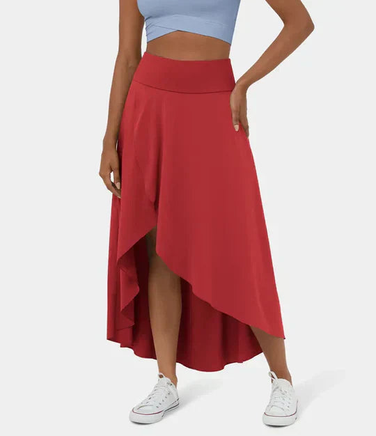 Jupe longue et fluide de couleur rouge, avec une coupe asymétrique et une fente sur le côté. Un modèle élégant et léger, parfait pour un look estival moderne et décontracté, à associer avec un top court et des baskets blanches.