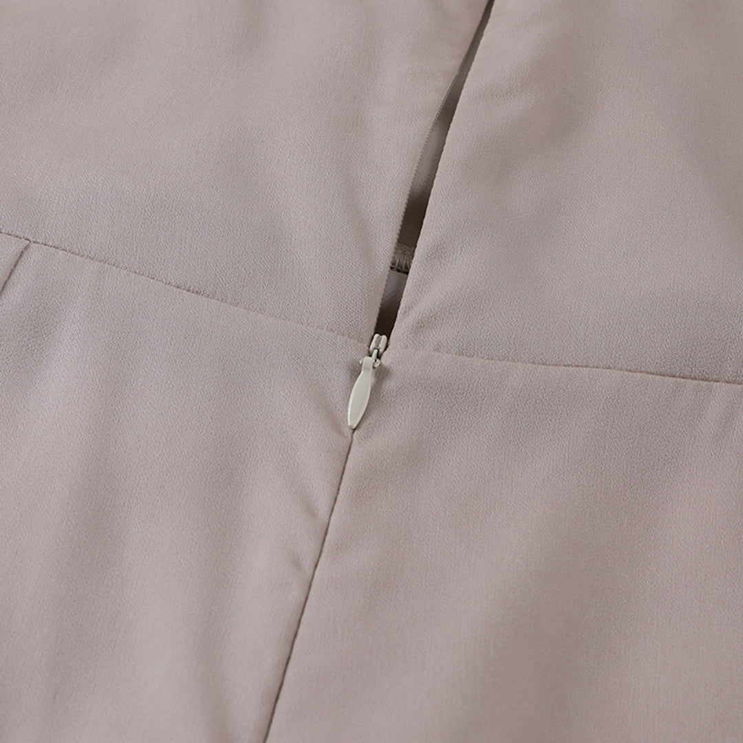 Vue rapprochée d’une fermeture éclair argentée sur une robe en satin beige clair. L’image met en valeur la texture fluide et élégante du tissu ainsi que la finition soignée de la couture, illustrant la qualité et le raffinement du vêtement.