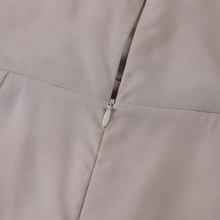Vue rapprochée d’une fermeture éclair argentée sur une robe en satin beige clair. L’image met en valeur la texture fluide et élégante du tissu ainsi que la finition soignée de la couture, illustrant la qualité et le raffinement du vêtement.