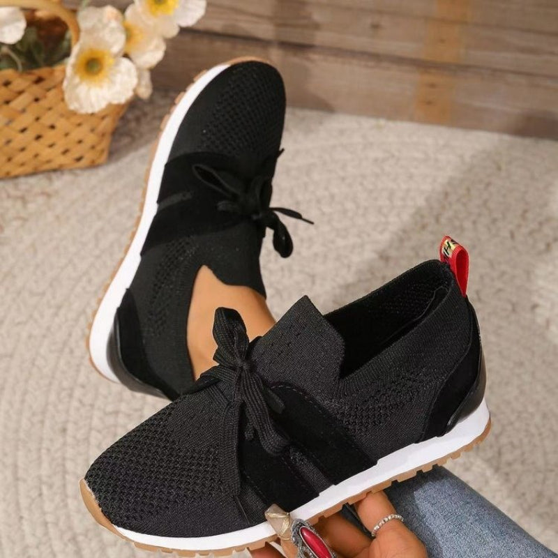 Baskets femme noires en maille respirante avec lacets, semelle plate blanche et extérieure gomme, style moderne et confortable.